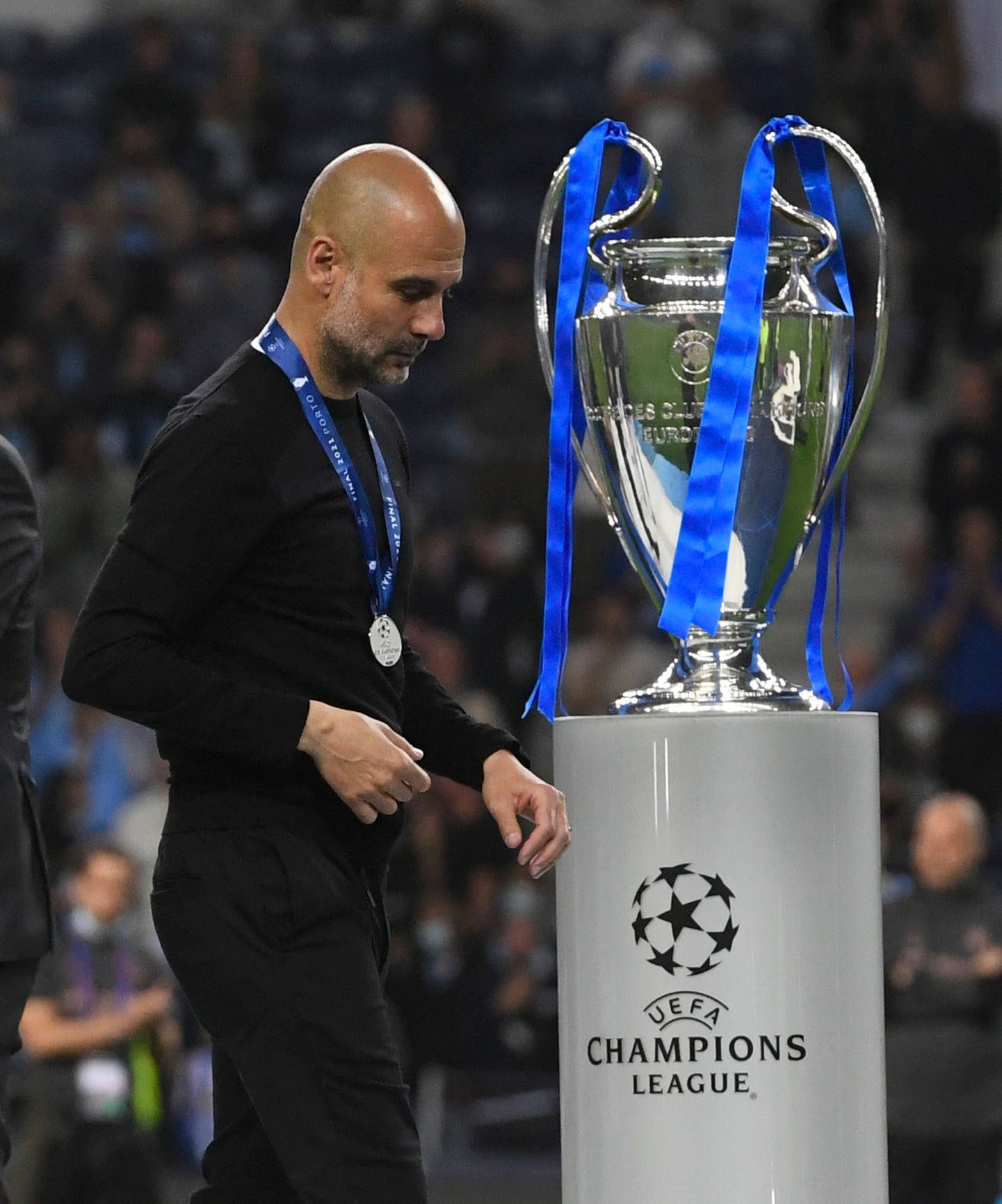 Guardiola walks past the Champions League trophy.