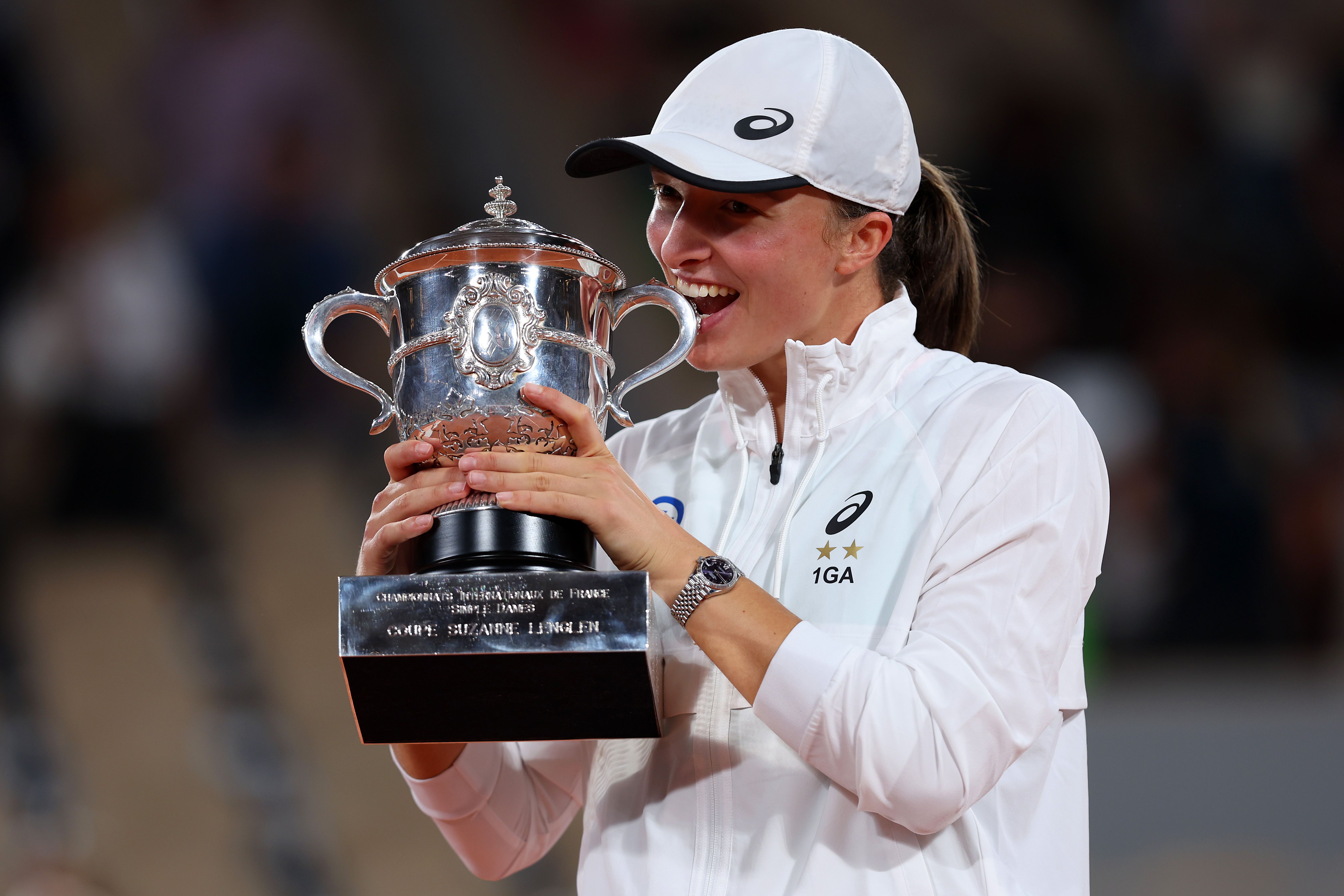 Iga Świątek bites the trophy to celebrate winning the 2022 French Open