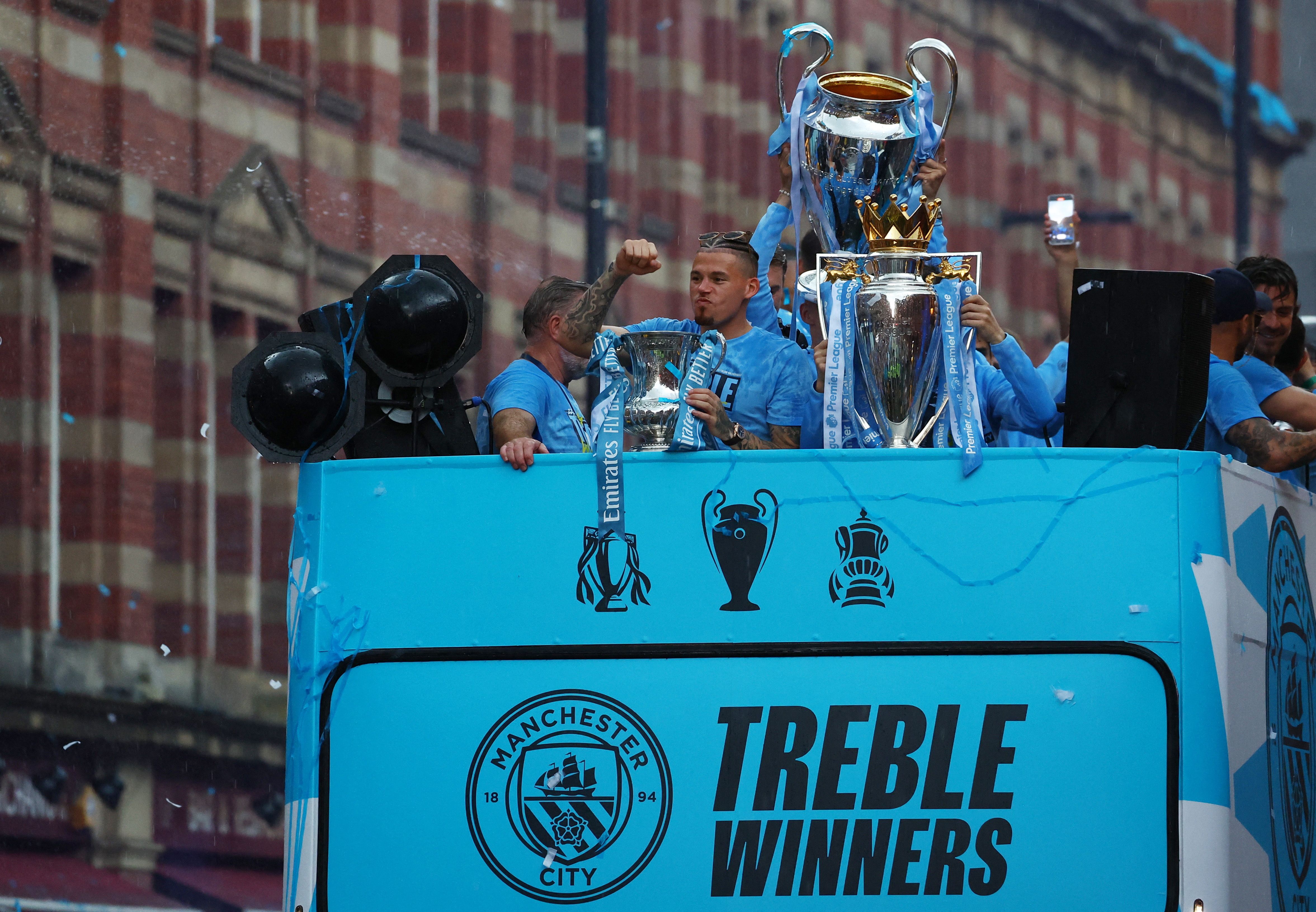 Manchester City's Kalvin Phillips celebrates with the FA Cup trophy as the Champions League and Premier League trophies are pictured next to him.