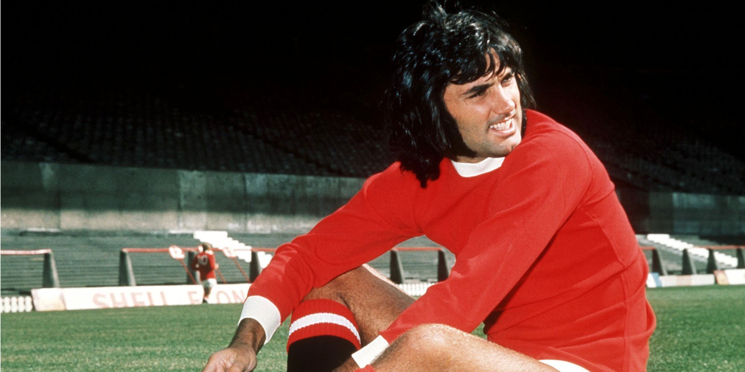 George Best reclining on a football pitch in his Manchester United kit