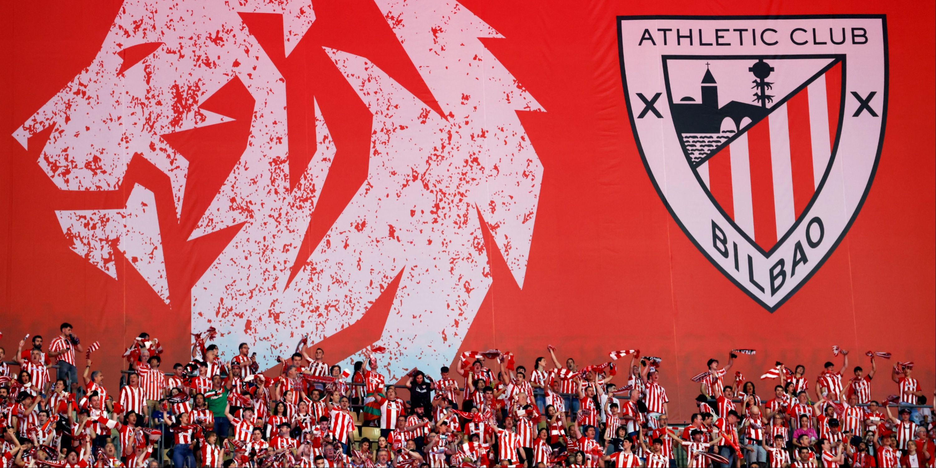 Athletic Bilbao fans celebrate against a backdrop featuring their club crest. 