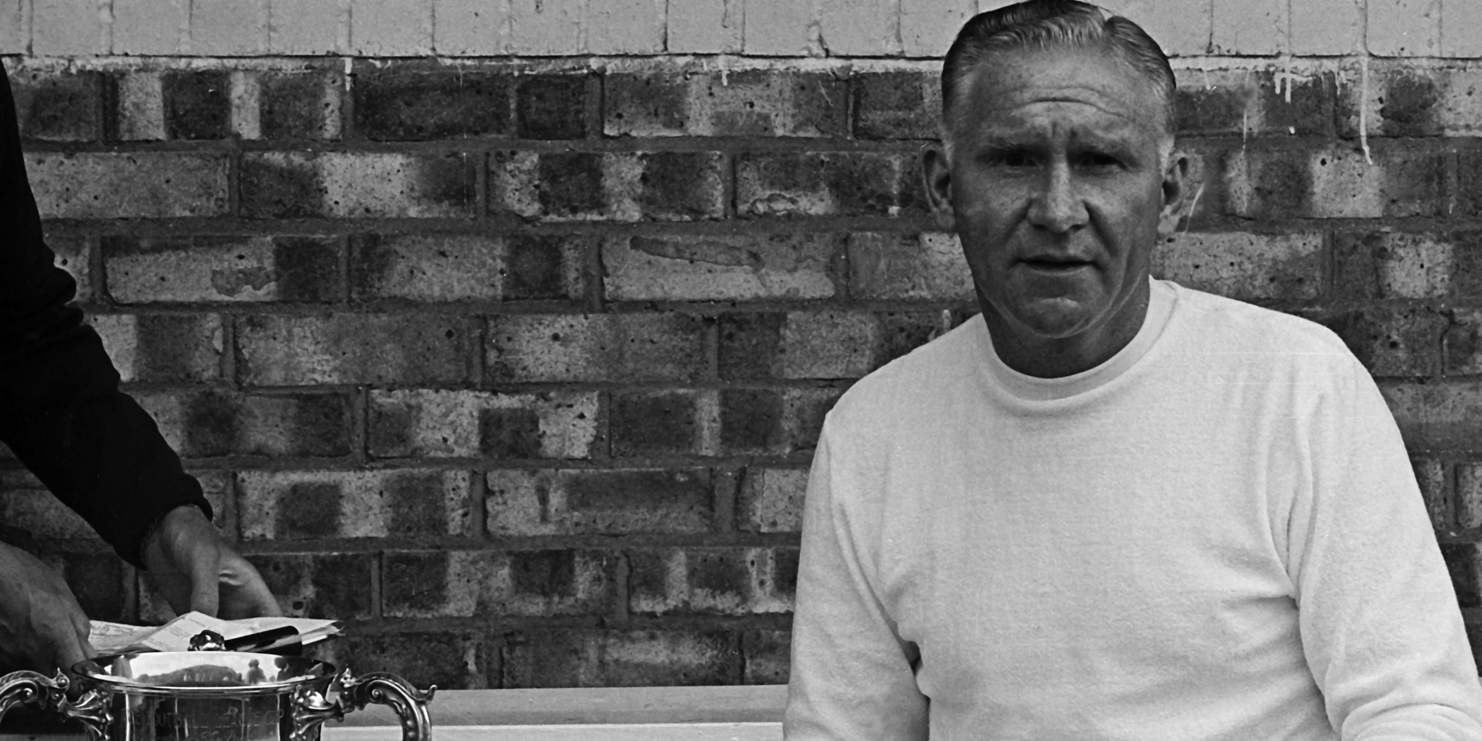 Bill Nicholson posing next to a trophy