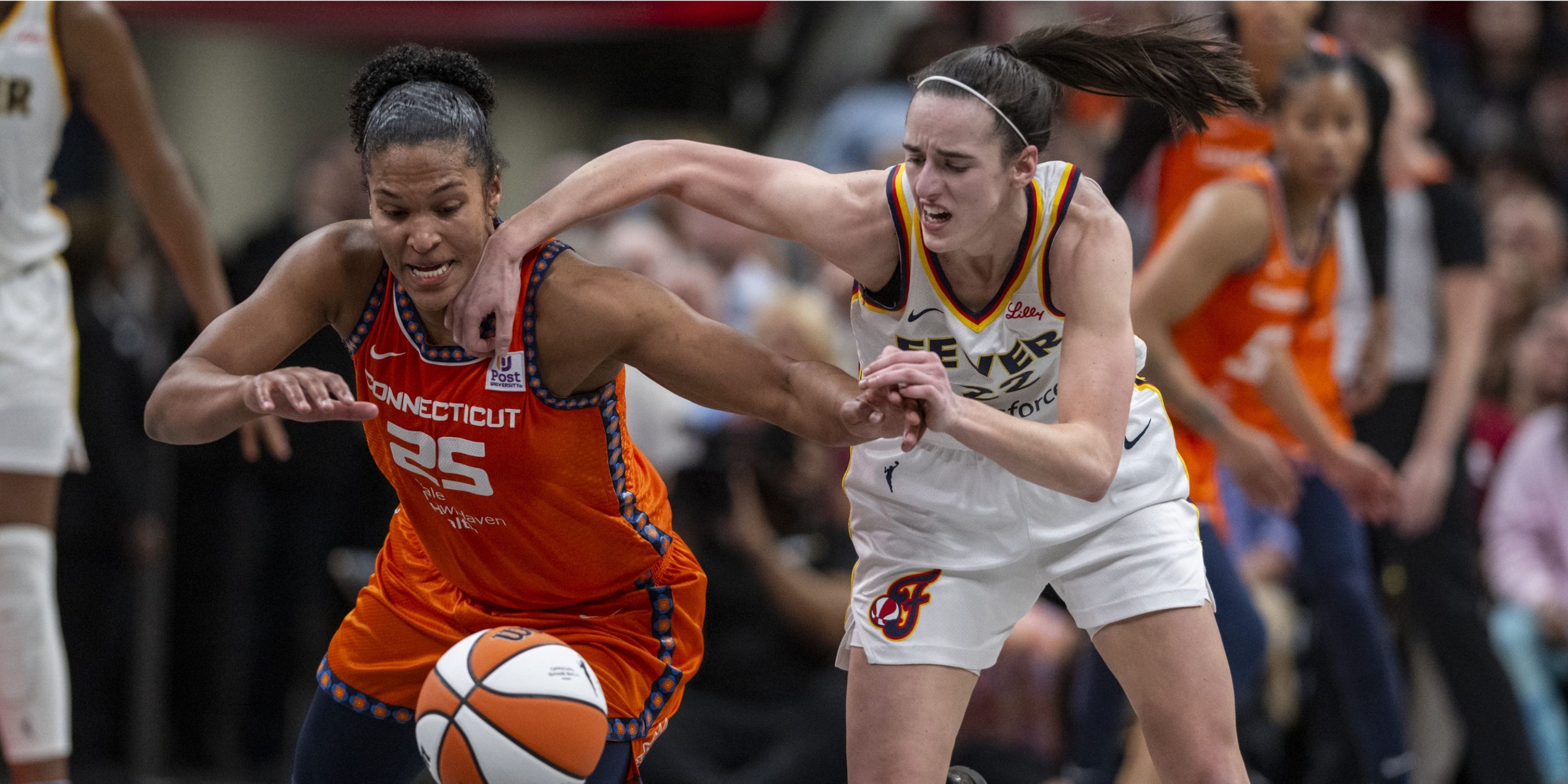 Alyssa Thomas of the Sun and Caitlin Clark of the Fever fight for a ball during a WNBA game.