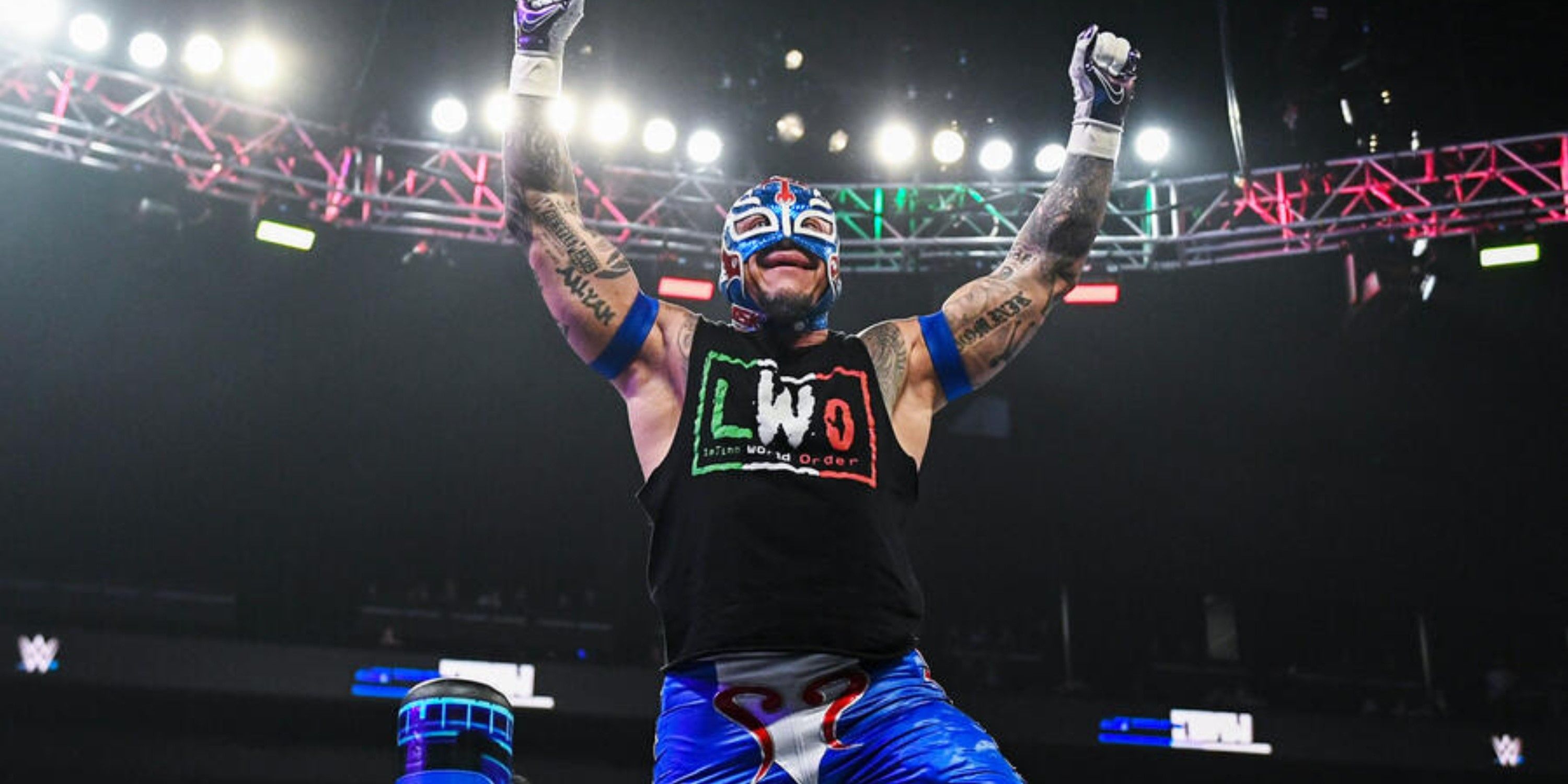 Rey Mysterio poses on the top rope wearing an LWO shirt