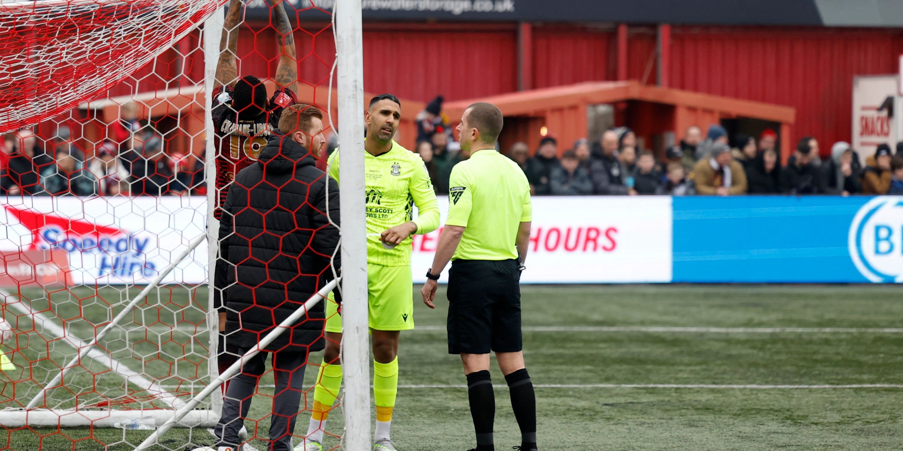 Tamworth's Jordan Cullinane-Liburd fixes the net as Tamworth's Jasbir Singh and referee Peter Bankes look on before the match