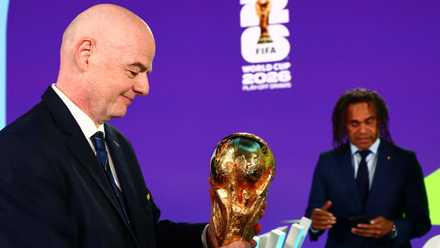 2025 FIFA president Gianni Infantino holds the World Cup trophy after the draw as former France player and 1998 FIFA World Cup winner Christian Karembeu is seen